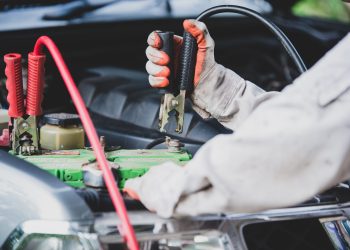 Car repairman wearing a white uniform standing and holding a wrench that is an essential tool for a mechanic